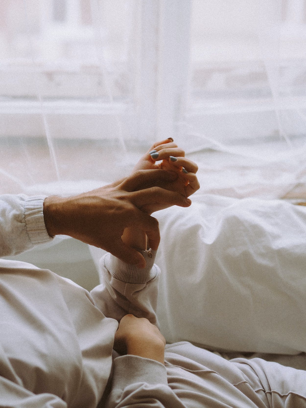 man woman holding each other's hands in bed.