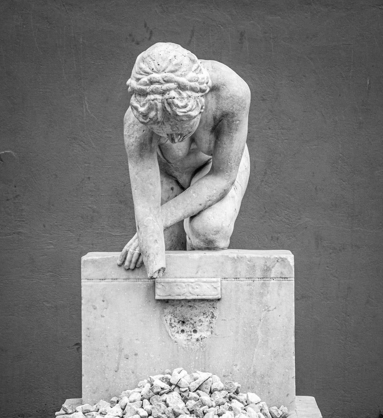 a statue of a woman looking down at rocks.